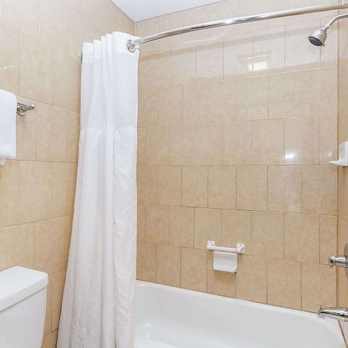 A bathroom with beige tiles features a bathtub, a white shower curtain, a towel on a rack, and a showerhead above the tub, ending the sentence.