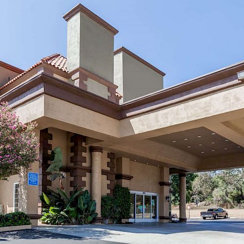 The image shows the entrance of a large building, likely a hotel, with a covered driveway and some cars parked nearby.