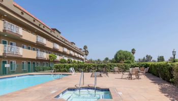 The image shows a hotel courtyard with a swimming pool, hot tub, and outdoor seating area surrounded by a well-maintained garden.