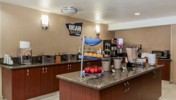 The image shows a breakfast buffet area with food, fruits, coffee machines, and condiments on a granite counter.