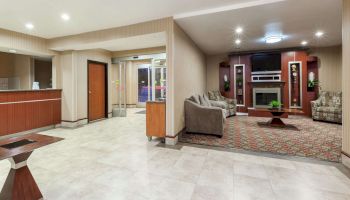 This image shows a hotel lobby with a reception desk, seating area with sofas, a coffee table, and a fireplace. The space is well-lit and modern.