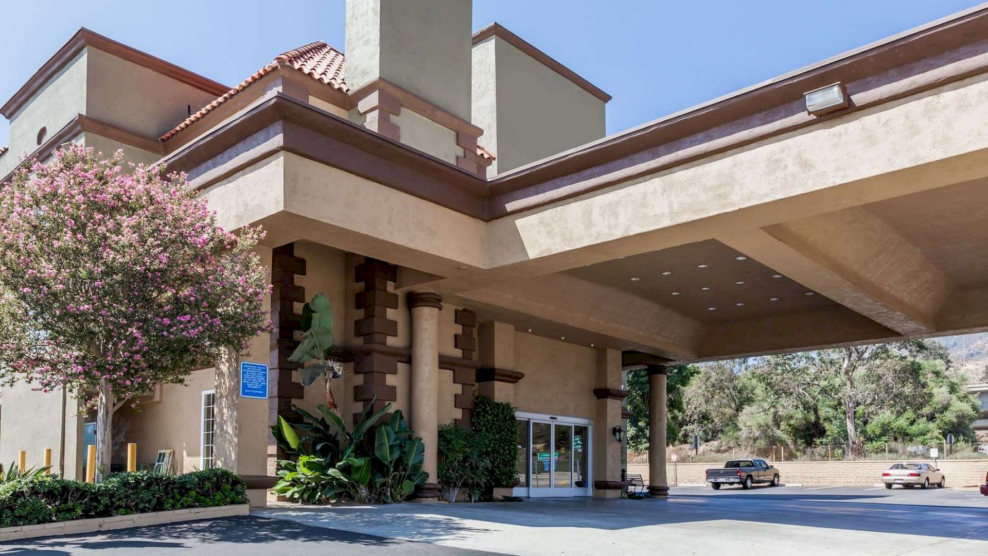 The image shows the exterior of a building, likely a hotel or inn, with a covered entrance and a second floor. Two cars are parked nearby.
