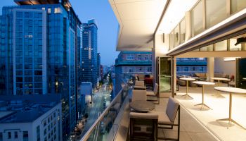 Modern cityscape with high-rise buildings, viewed from a balcony with seating and tables, during twilight.