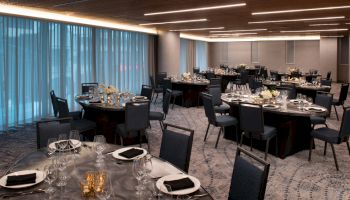 The image shows an elegantly set banquet hall with multiple round tables, each prepared with cutlery, plates, and candles for an event.