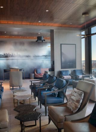 A comfortable lounge area with numerous seating options, large windows offering a waterfront view, and a wall mural of a city skyline ends the sentence.