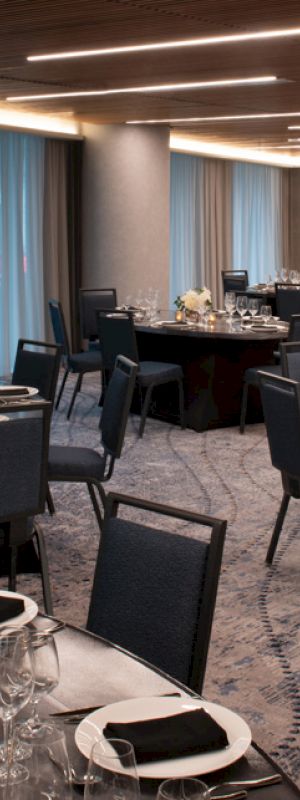 A banquet hall with round tables set with glassware, cutlery, and floral centerpieces, ready for an event.