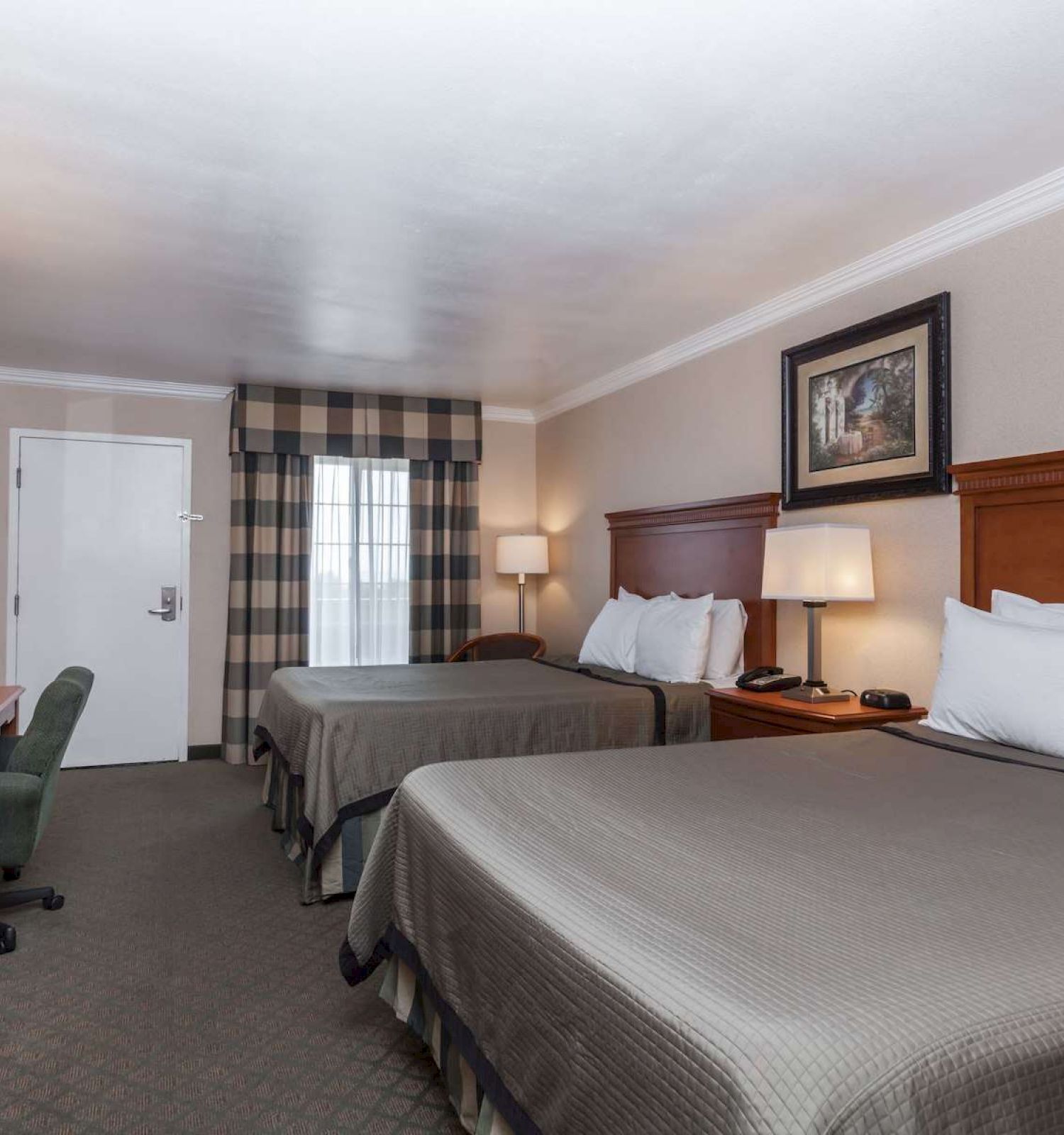 A hotel room with two double beds, a desk, a flat-screen TV, and a window covered by plaid curtains.