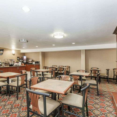 The image depicts a clean, well-lit dining area with tables and chairs, a television, and a fireplace. The room also has a food and drink station.